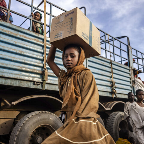 A Sudanese girl who have fled from the war in Sudan with her family carry a box with some of her belongings after arriving at a Transit Centre for refugees in Renk, on February 13, 2024.More than 550,000 people have now fled from the war in Sudan to South Sudan since the conflict exploded in April 2023, according to the United Nations. South Sudan, that has itself recently come out of decades of war, was facing a dire humanitarian situation before the war in Sudan erupted and it is feared to not have the re